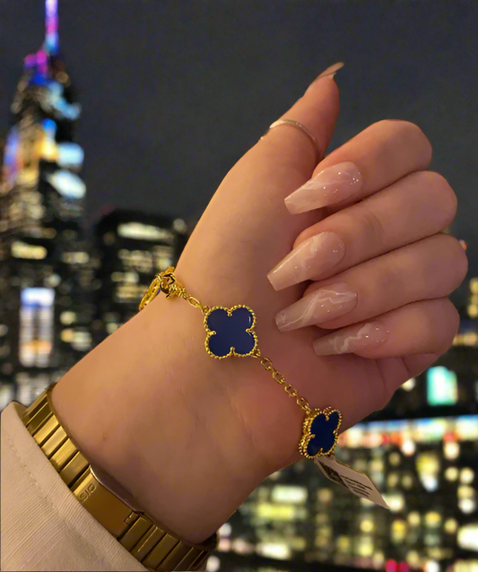 Hand wearing a gold bracelet with blue clover-shaped charms against a blurred background