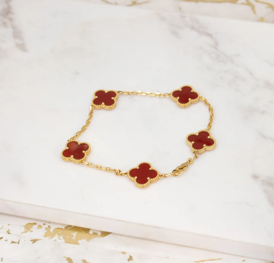 Gold bracelet with red clover-shaped charms on a white fabric background