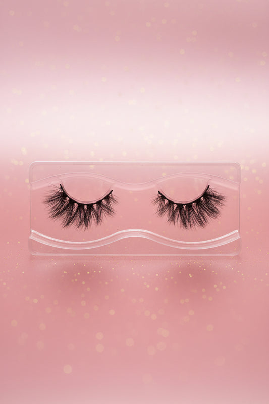 A pair of black false eyelashes in a clear plastic tray, placed on a light wood grain surface.