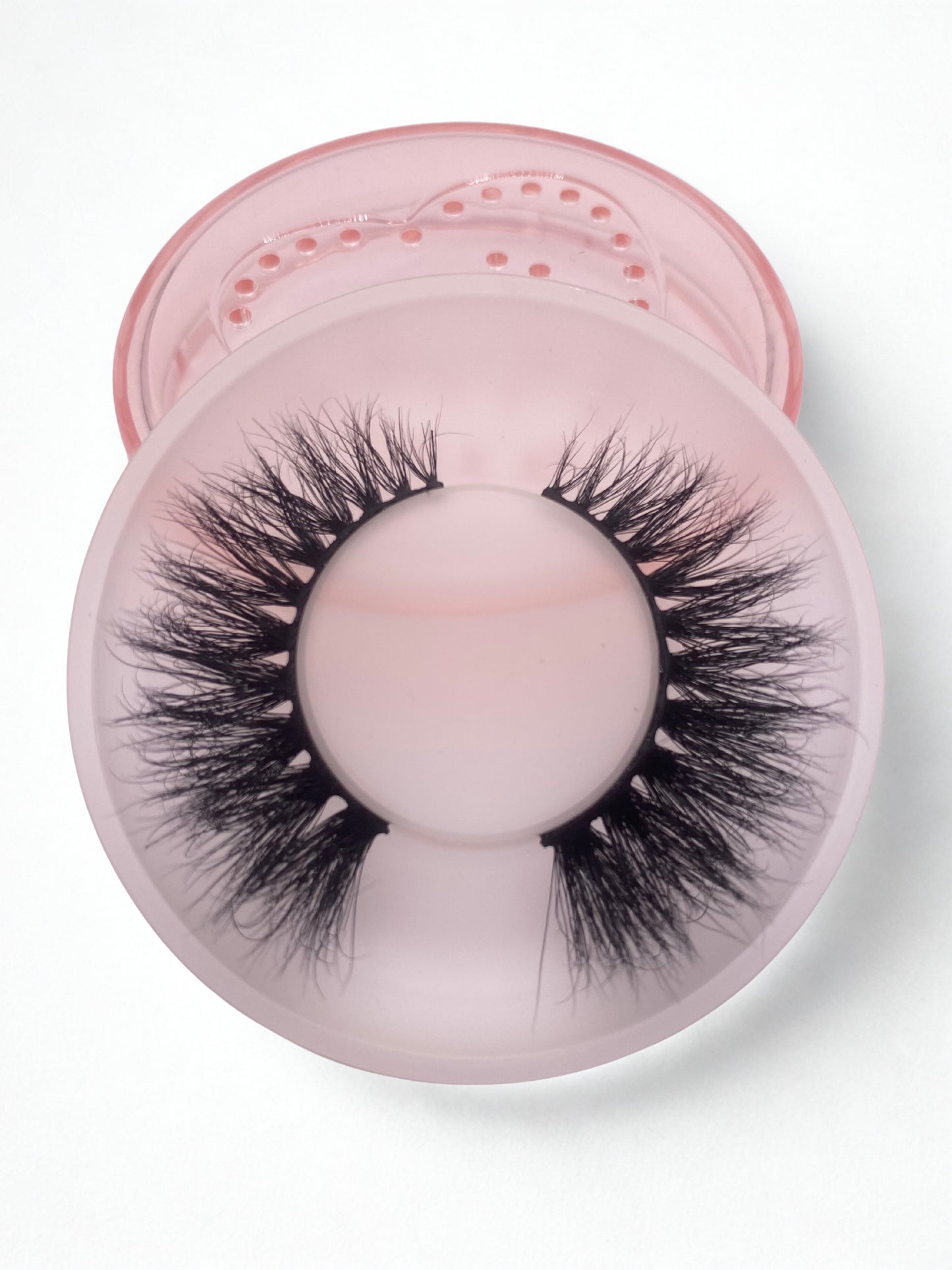 Pair of mink false eyelashes on a pink cushion with a clear container on a white background