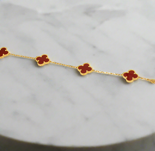 Gold bracelet with red clover-shaped stones on a white fabric background